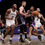 Jan 27, 2025; Brooklyn, New York, USA; Sacramento Kings guard De'Aaron Fox (5) drives to the basket past Brooklyn Nets center Day'Ron Sharpe (20) and guards Tyrese Martin (13) and D'Angelo Russell (1) and Kings forward Domantas Sabonis (11) during the third quarter at Barclays Center. Mandatory Credit: Brad Penner-Imagn Images